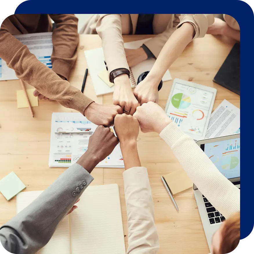 Diverse team members sitting around a table putting their fists together in a gesture of unity