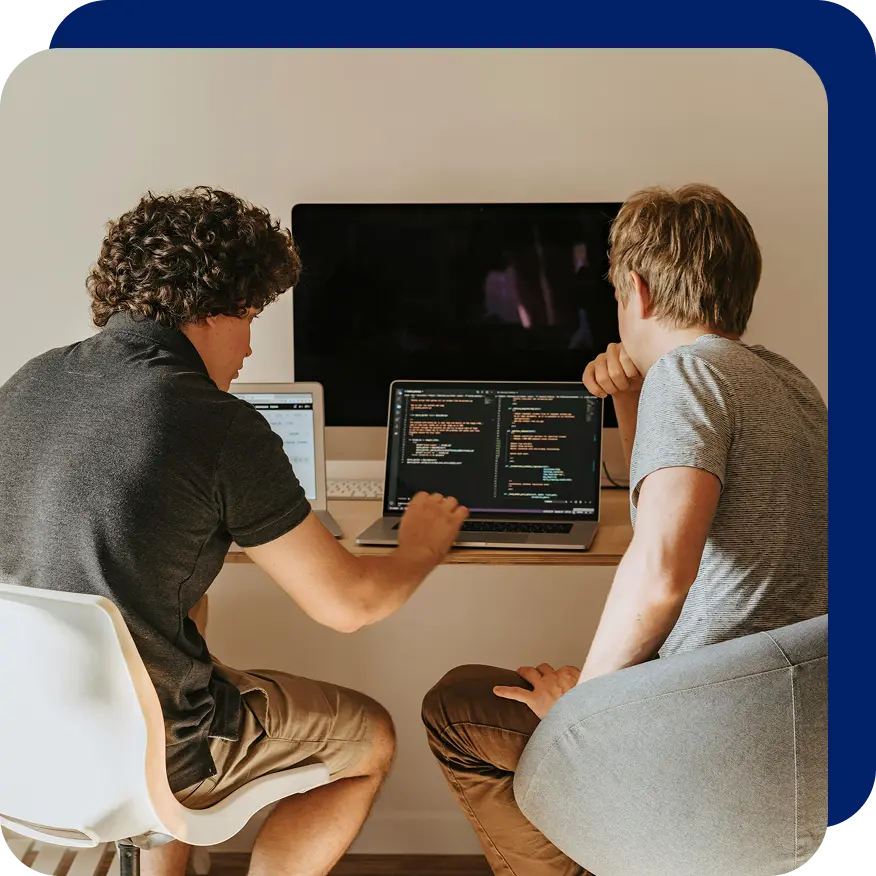 Two male developers collaborating at a desk with multiple laptops and a large monitor