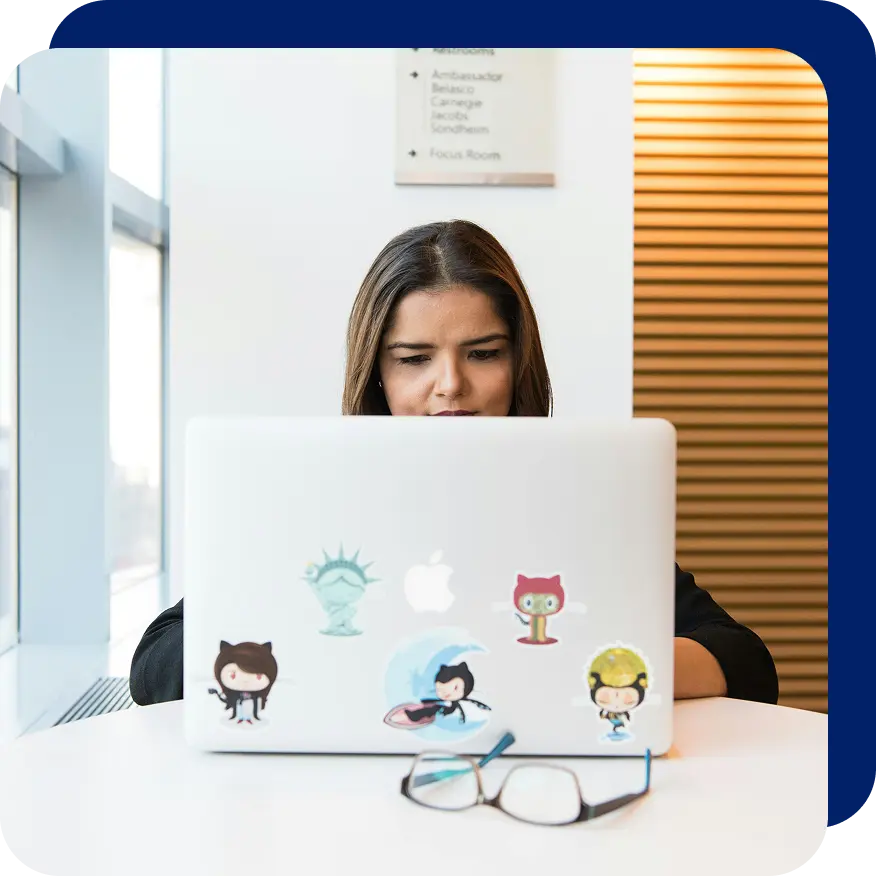 Woman working intently on a laptop decorated with GitHub and other tech-related stickers