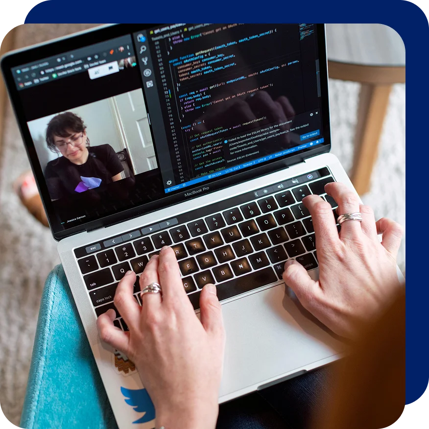 Person typing on a laptop during a video call, with code displayed on one side of the screen and a team member visible on the other, representing remote DevOps or cloud collaboration