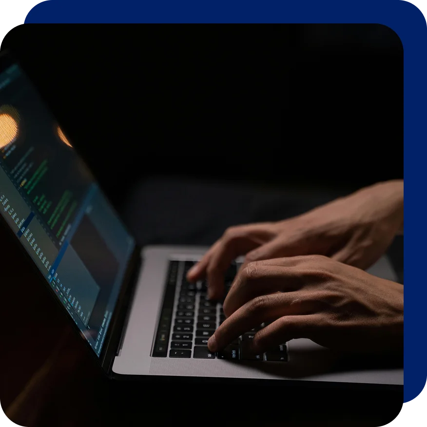 Close-up of hands typing code on a laptop in a dark environment, with the screen displaying a programming interface, symbolizing digital transformation or late-night software development