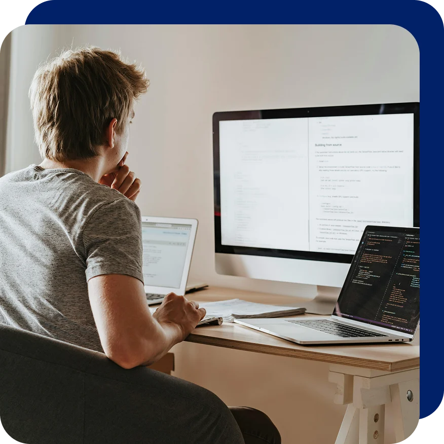 Person sitting at a desk with multiple screens displaying code and documentation, appearing deep in thought, representing work related to GDPR compliance or secure software development