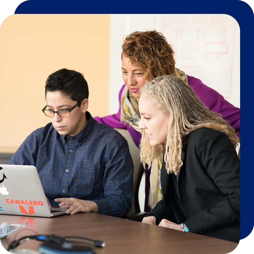 Three professionals gathered around a laptop during a meeting, reviewing information on the screen with focused expressions, symbolizing collaboration on SEO strategy