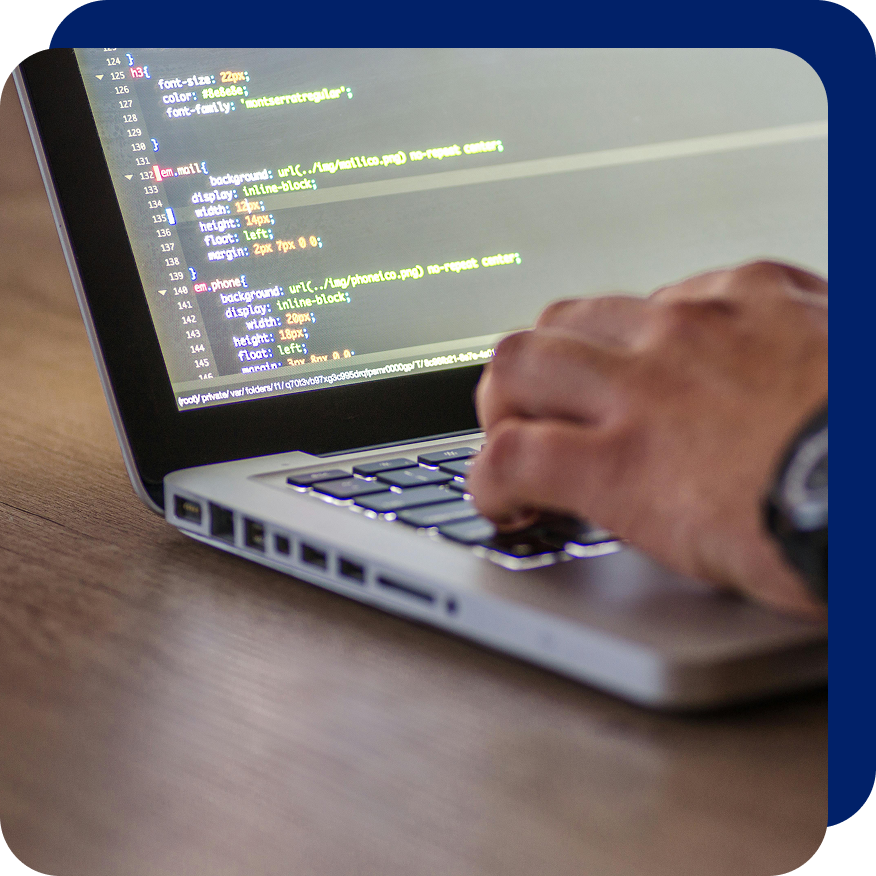 Close-up of a person coding CSS on a laptop, showing styled HTML elements and a hand typing on the keyboard.